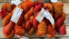 Närbild på garnhärvor i orangea och röda toner på träbord – Teija - Textil i Järfälla